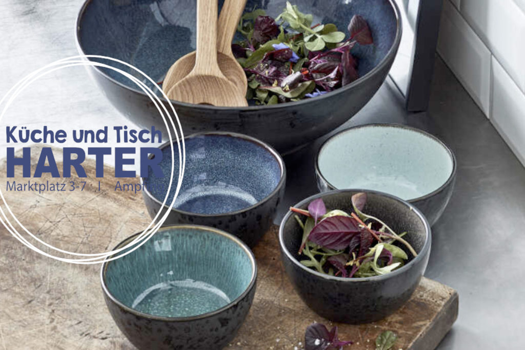 Ein Satz Keramikschüsseln in verschiedenen Größen, gefüllt mit Grünzeug, steht auf einem hölzernen Schneidebrett. In der größten Schüssel liegt ein hölzernes Salatbesteck. Der Textüberzug lautet „Küche und Tisch Harter, Marktplatz 3-7, Ampt.