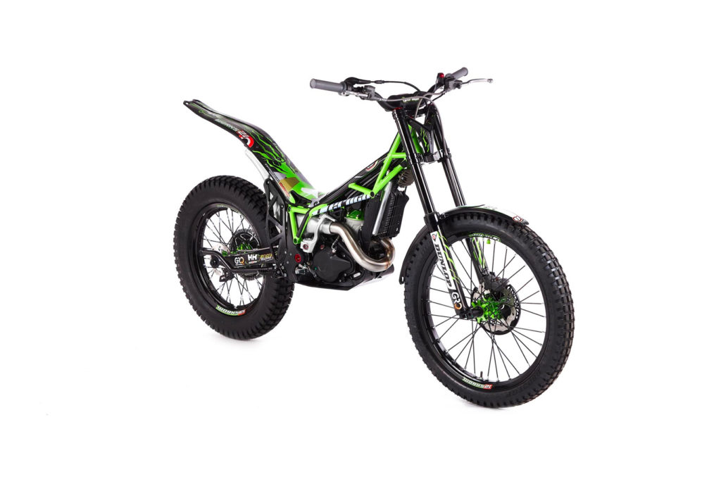 Auf einem weißen Hintergrund ist ein grün-schwarzes Trial-Motorrad mit leichtem Rahmen und robusten Reifen zu sehen. Das Motorrad ist mit einem Branding versehen und hat ein Design mit hoher Bodenfreiheit, das für Geländefahrten und wendiges Fahren gedacht ist.