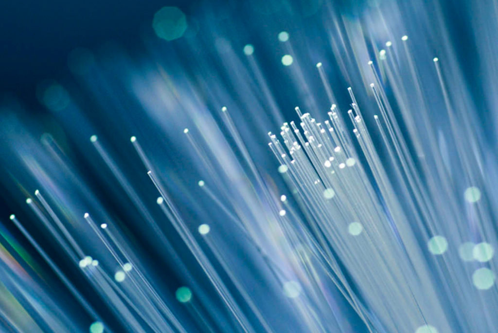 Nahaufnahme von Glasfaserkabeln, die vor einem weichen, unscharfen Hintergrund in weißem und blauem Licht leuchten. Die Stränge wirken zart und sind über das Bild verteilt, wodurch ein schillernder Effekt entsteht.