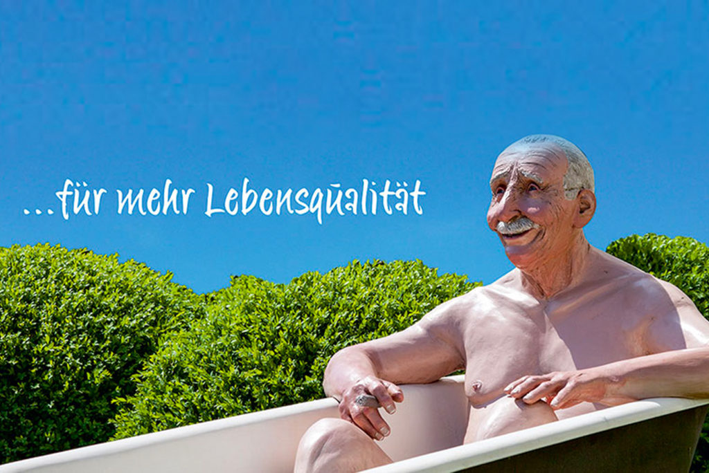 Ein älterer Mann mit zufriedenem Gesichtsausdruck entspannt in einer Badewanne im Freien, umgeben von Grün, über ihm ein klarer blauer Himmel. Der Text lautet „für mehr Lebensqualität“.