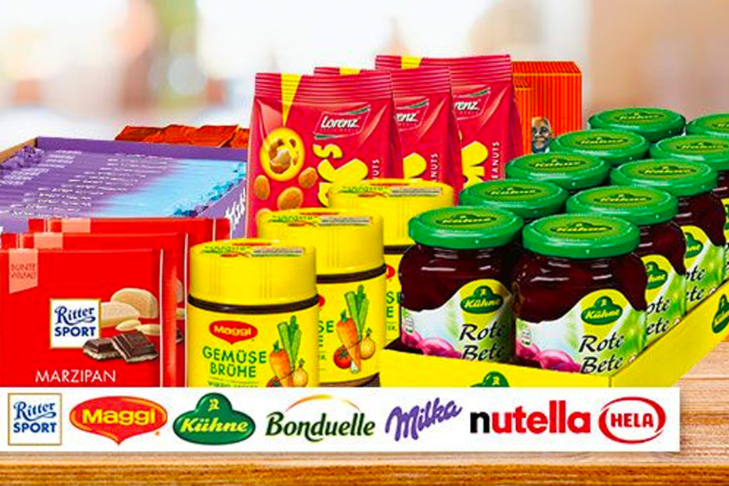Eine Ausstellung verschiedener Lebensmittel, darunter Ritter Sport-Schokolade, Maggi-Gewürz, Kühne Gemüsebrühe und Rote Bete, Lorenz-Chips, Bonduelle-Artikel, Milka-Schokolade, Nutella und Hela-Sauce. Die Artikel sind für die Präsentation von Werbeartikeln arrangiert.