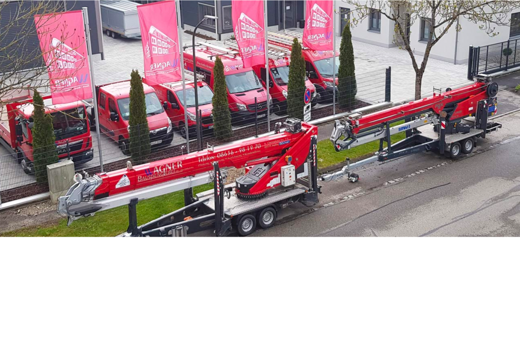 Rote Baukräne sind auf Anhängern montiert und neben einer Reihe roter Nutzfahrzeuge auf einem Parkplatz geparkt. Auf Fahnen neben den Fahrzeugen sind ein Logo und ein Text zu sehen. Im Hintergrund sind Bäume und ein Gebäude zu sehen.