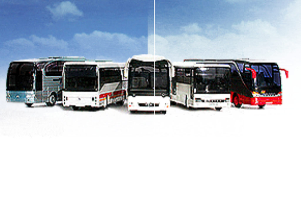 Eine Reihe von fünf Spielzeugbussen ist aufgestellt, jeder mit einem anderen Design und einer anderen Farbe, darunter Silber, Weiß mit roten Streifen und Weiß mit schwarzen und roten Details, vor einem blauen Himmel mit Wolken im Hintergrund.