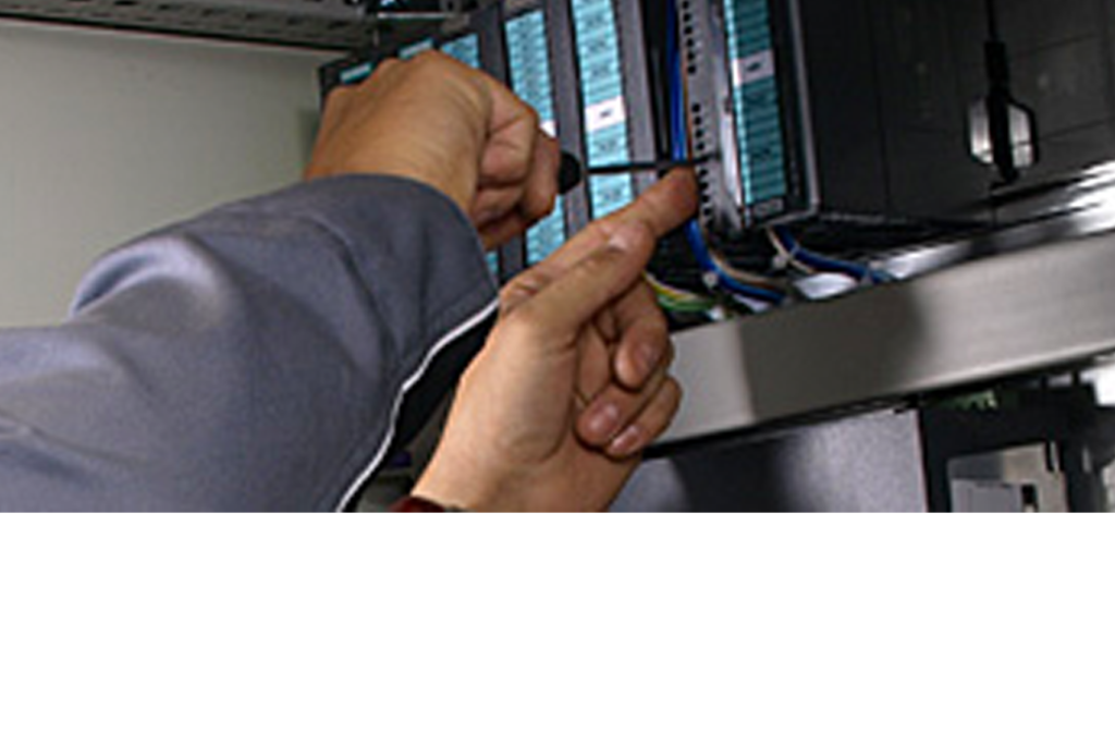 Person, die eine Jacke trägt und Kabel oder Komponenten in einem Server-Rack einstellt. Die Aufnahme konzentriert sich auf ihre Hände und die Ausrüstung und deutet auf eine technische oder IT-Umgebung hin.