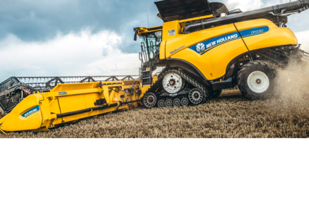 Ein gelber Mähdrescher vom Typ New Holland CR10.90 ist unter bewölktem Himmel auf einem Feld im Einsatz. Die Maschine ist mit Raupenketten ausgestattet und bewegt sich durch das abgeerntete Feld, wobei sie Staub aufwirbelt.