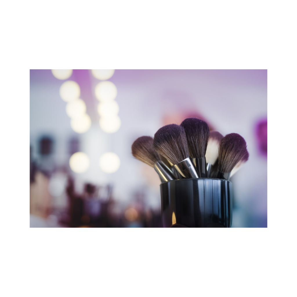 Ein Set Make-up-Pinsel in einem schwarzen Halter mit verschwommenen hellen Lichtern im Hintergrund, die eine sanfte, farbenfrohe Atmosphäre schaffen.