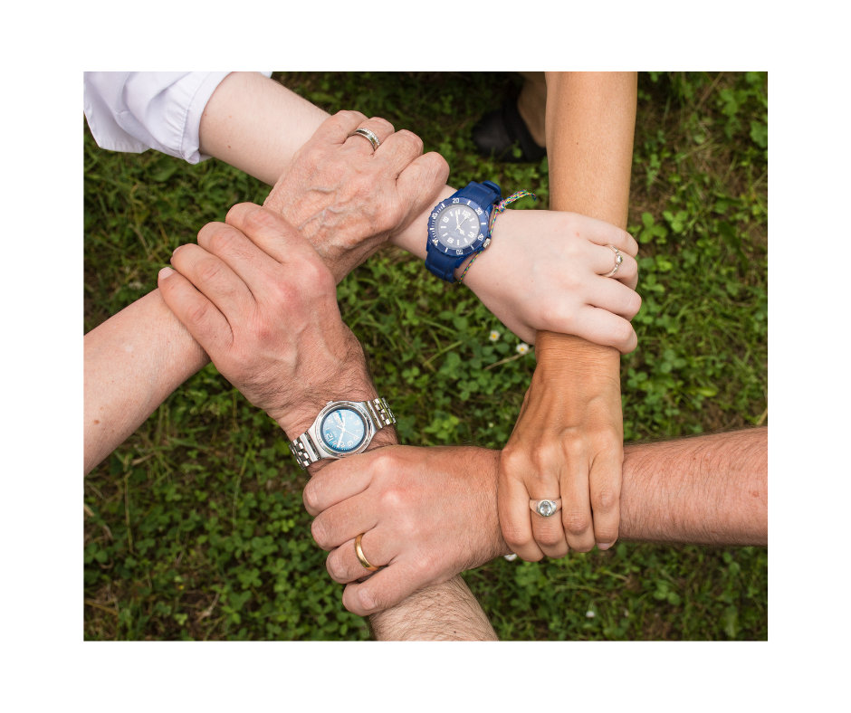 Sechs Hände mit unterschiedlichen Hauttönen bilden über dem Gras einen Kreis. Jeder trägt eine andere Uhr und einen anderen Ring und symbolisiert damit Einigkeit und Teamwork.