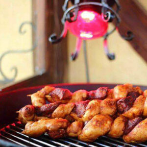 Ein Grill mit mehreren gewürzten Hähnchenteilen, die unter einer roten Wärmelampe garen und eine warme und einladende Atmosphäre schaffen.