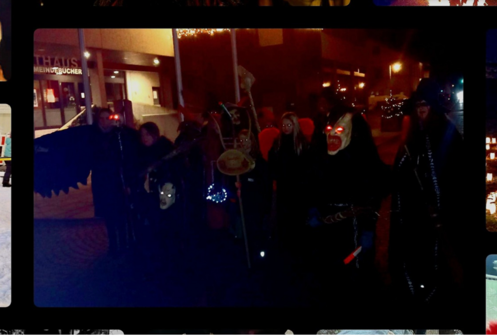 Eine Gruppe von Menschen in dunklen, gruseligen Kostümen und leuchtenden Masken posiert zusammen auf einer schwach beleuchteten nächtlichen Straße, mit Gebäuden und Lichtern im Hintergrund.