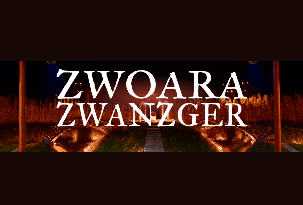 Weißer Text mit der Aufschrift "ZWOARA ZWANZGER" steht über einer dunklen Szene im Freien mit einem hölzernen Weg, leuchtenden orangefarbenen Lichtern und hohem Gras im Hintergrund.