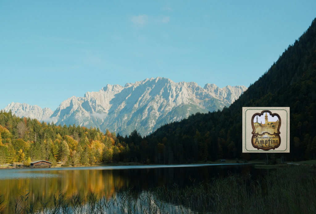 In einem ruhigen See spiegeln sich Herbstbäume und eine Bergkette unter einem klaren blauen Himmel. Am Ufer steht eine kleine Hütte. Ein verziertes Logo in Braun und Gold mit dem Wort "Amorfino" ist unten rechts angebracht.