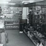 Schwarz-Weiß-Foto des Innenraums eines Baumarkts, auf dem verschiedene Werkzeuge und Geräte in Regalen und an Wandhalterungen ausgestellt sind.