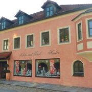 Ein langes, pfirsichfarbenes, zweistöckiges Gebäude mit einem Laden im Erdgeschoss und dem Schriftzug „Küche und Tisch Harter“ an der Fassade.