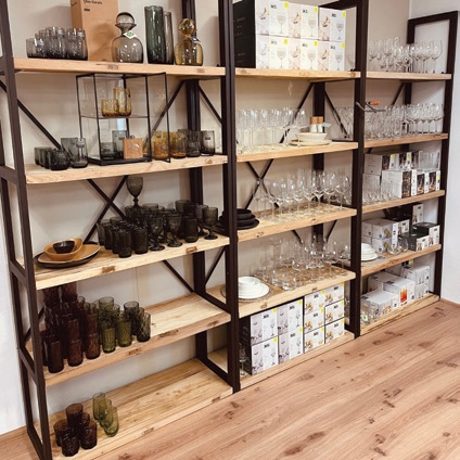 Hohe Metallregale, in denen verschiedene Sets aus Trinkgläsern, Stielgläsern, Schalen und in Kartons verpacktem Küchengeschirr ausgestellt sind.