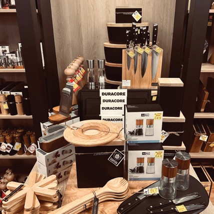 Eine Auslage in einem Küchengeschäft mit Messern mit Holzgriffen auf einem Messerblock, Salz- und Pfeffermühlen, Holzlöffeln und Küchenhelfern mit Preisschildern.