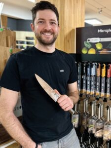 Florian Kupke hält ein Küchenmesser im Geschäft Küche und Tisch Harter