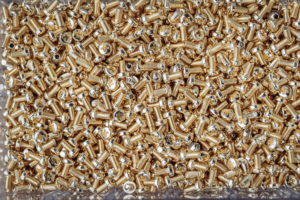 Eine Ansammlung zahlreicher kleiner, glänzender Goldschrauben mit Kreuzschlitzköpfen, die dicht beieinander liegen und eine strukturierte, metallische Oberfläche bilden.
