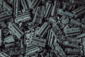Ein Stapel grüner mechanischer Kunststoffteile, bestehend aus einer Vielzahl rechteckiger Komponenten mit mehreren Löchern und Rillen. Die Teile sind zufällig gestapelt, wodurch ein strukturiertes und geschichtetes Muster entsteht.